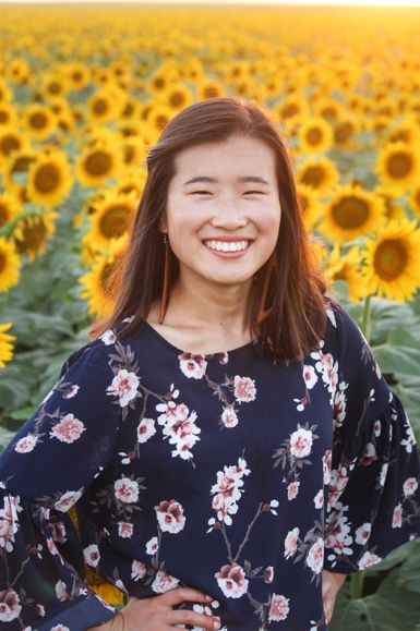 A person smiling in front of a field of yellow flowers

Description automatically generated with medium confidence